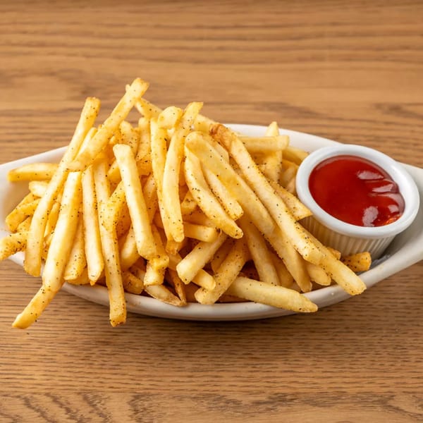 Crispy golden french fries seasoned with pepper, served in a white dish with a side of ketchup.