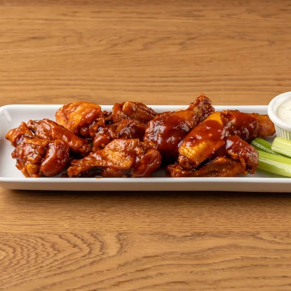Plate of saucy chicken wings with celery sticks and a side of ranch dressing.