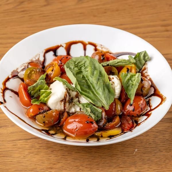 Caprese salad with cherry tomatoes, mozzarella, fresh basil, and balsamic glaze in a white bowl.