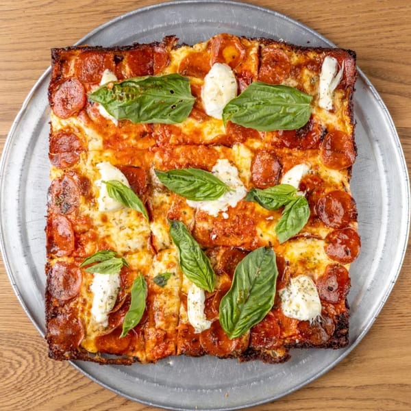 Square pepperoni pizza with fresh basil and dollops of ricotta cheese on a metal pan.