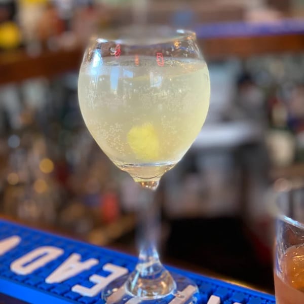 A sparkling white wine or cocktail in a stemmed glass with a lemon slice, on a bar.