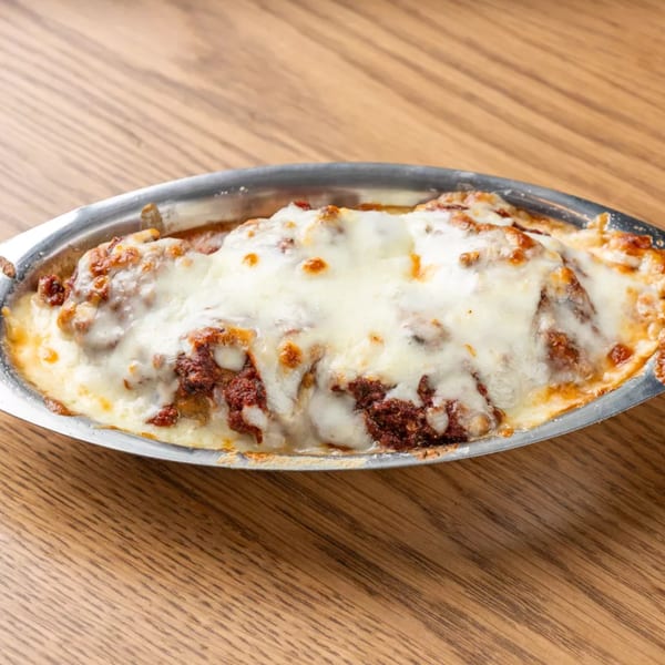 Baked lasagna with melted cheese and meat sauce in a silver dish on a wooden table.