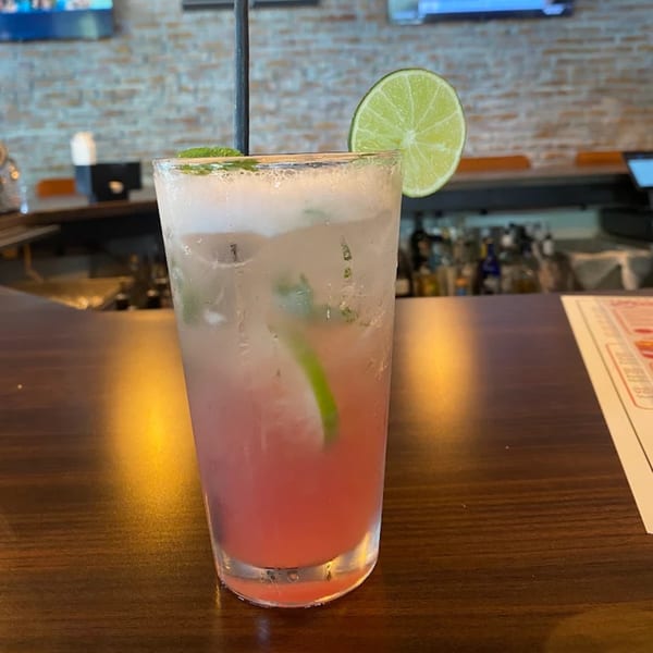 A refreshing pink cocktail with a lime slice and mint garnish sits on a wooden bar.