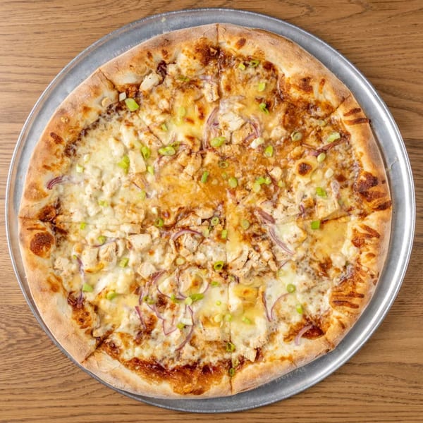 Overhead view of a whole BBQ chicken pizza with red onions and green onions on a metal pan.