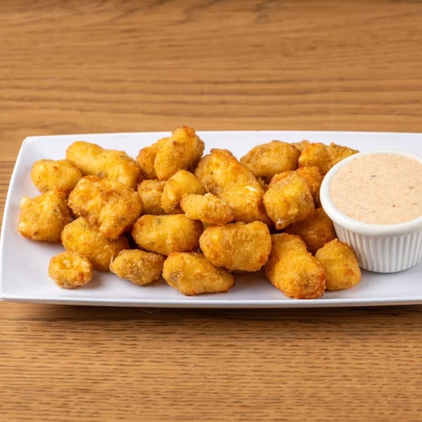 A white rectangular plate filled with golden-brown fried cheese curds and a side of dipping sauce.