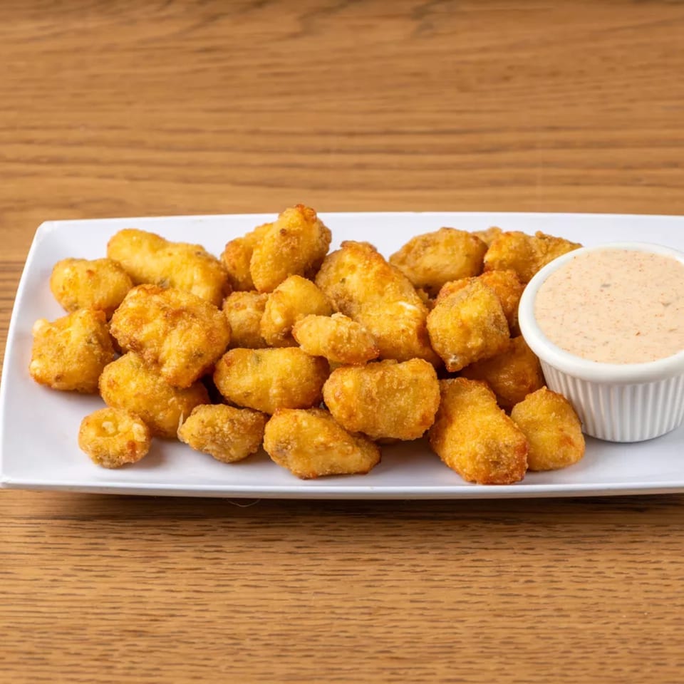 A white rectangular plate filled with golden-brown fried cheese curds and a side of dipping sauce.
