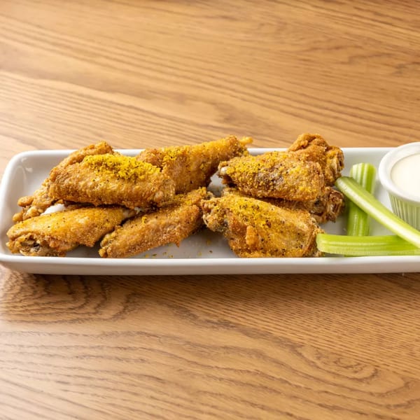 Crispy fried chicken wings seasoned with yellow spices, served with celery sticks and ranch dip.